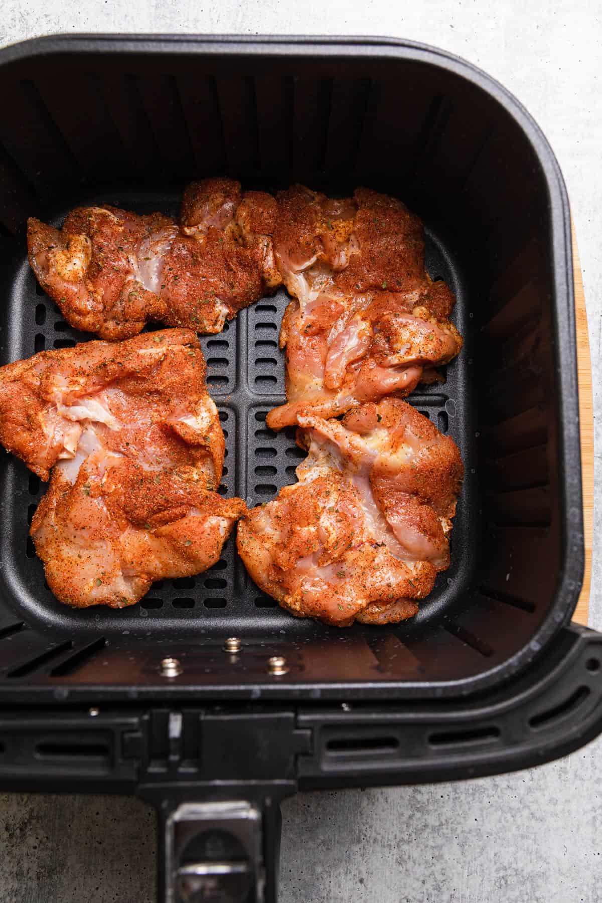 Placing raw chicken in the air fryer basekt.