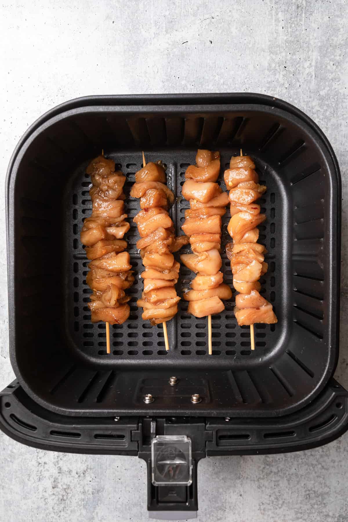Raw skewered chicken placed in an air fryer basket.