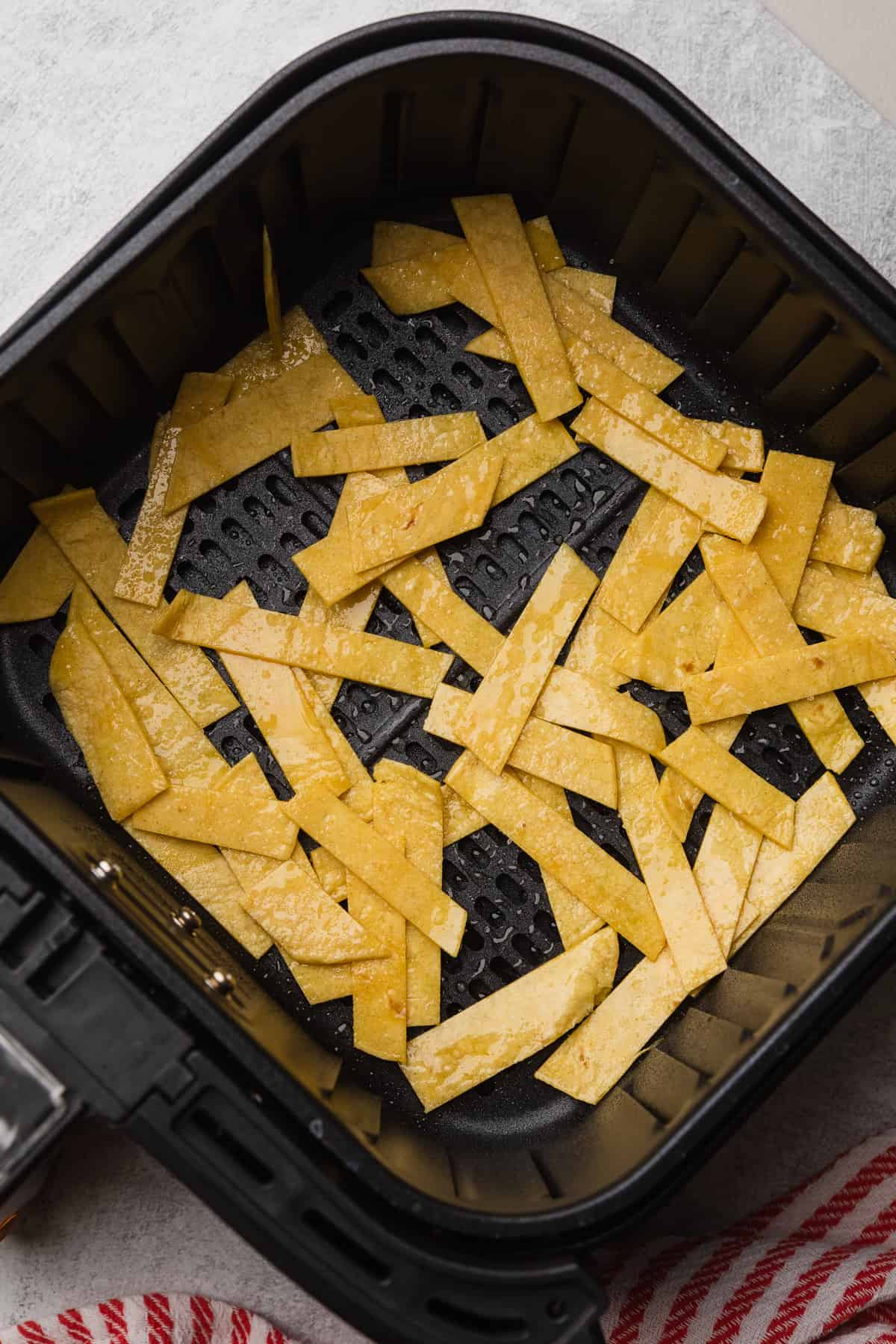 Corn tortilla strips in the air fryer basket before cooking.