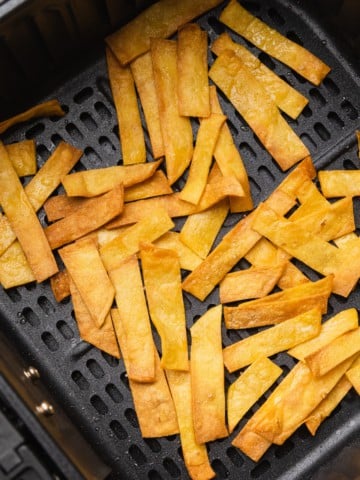 Cooked tortilla strips in air fryer basket.