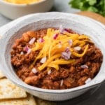 A bowl of texas roadhouse chili recipe topped with cheese and red onions.