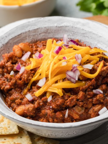 A bowl of texas roadhouse chili recipe topped with cheese and red onions.