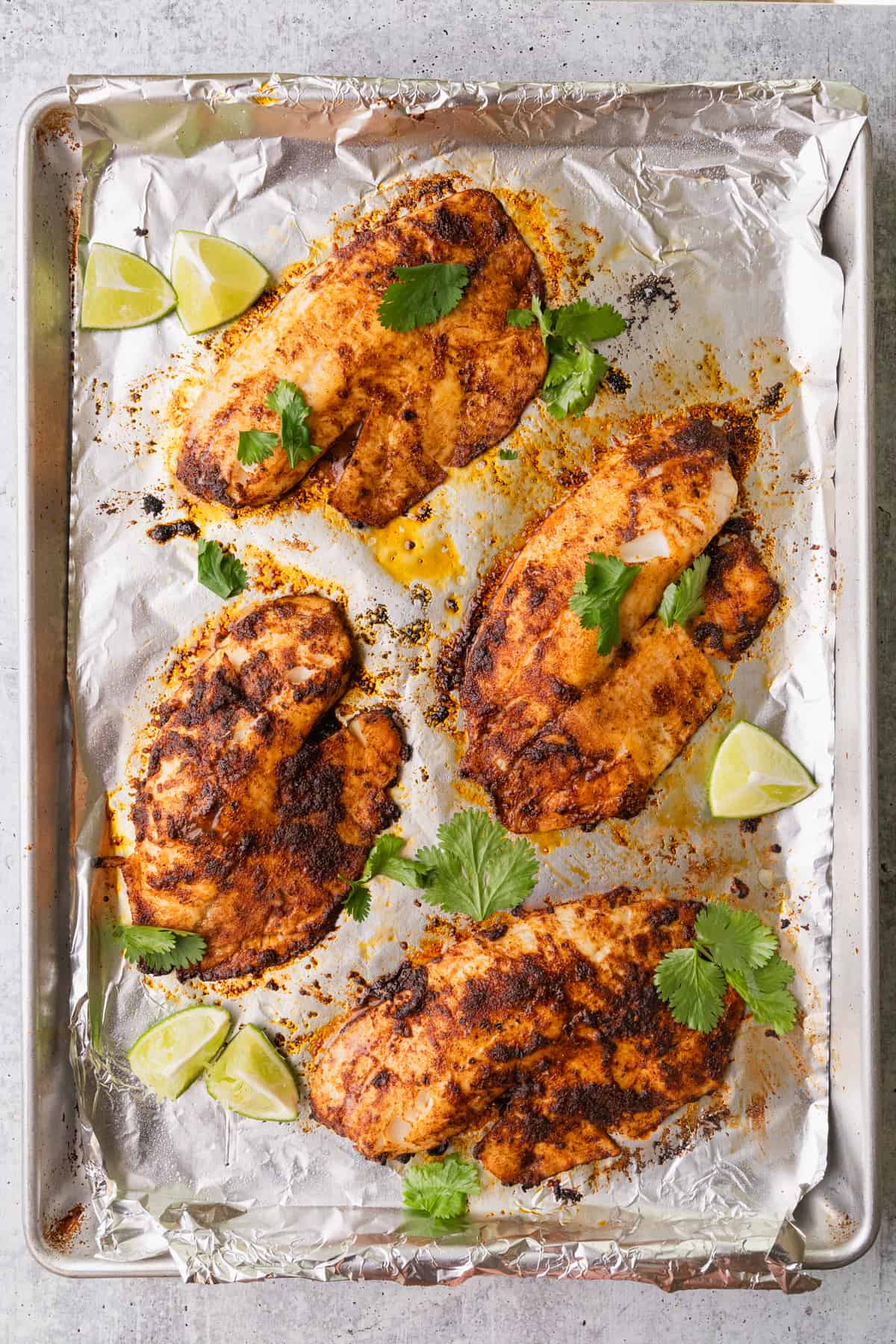 Baked blackened tilapia on a sheet pan with garnishes.