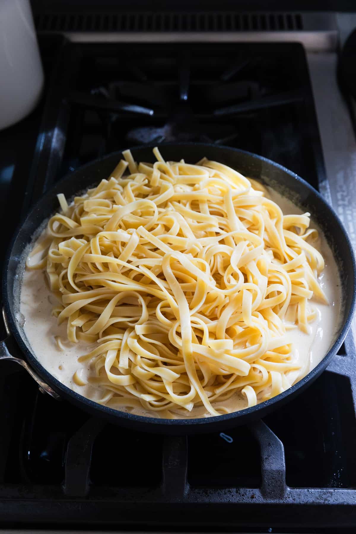 Adding cooked fettuccine noodles to alfredo sauce.