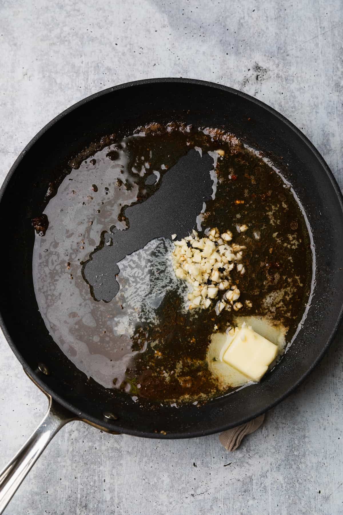 Adding garlic and butter to a pan to make the sauce fettuccine alfredo recipe.