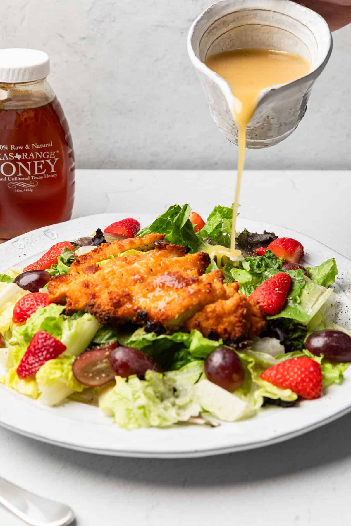 Pouring honey mustard over a salad.