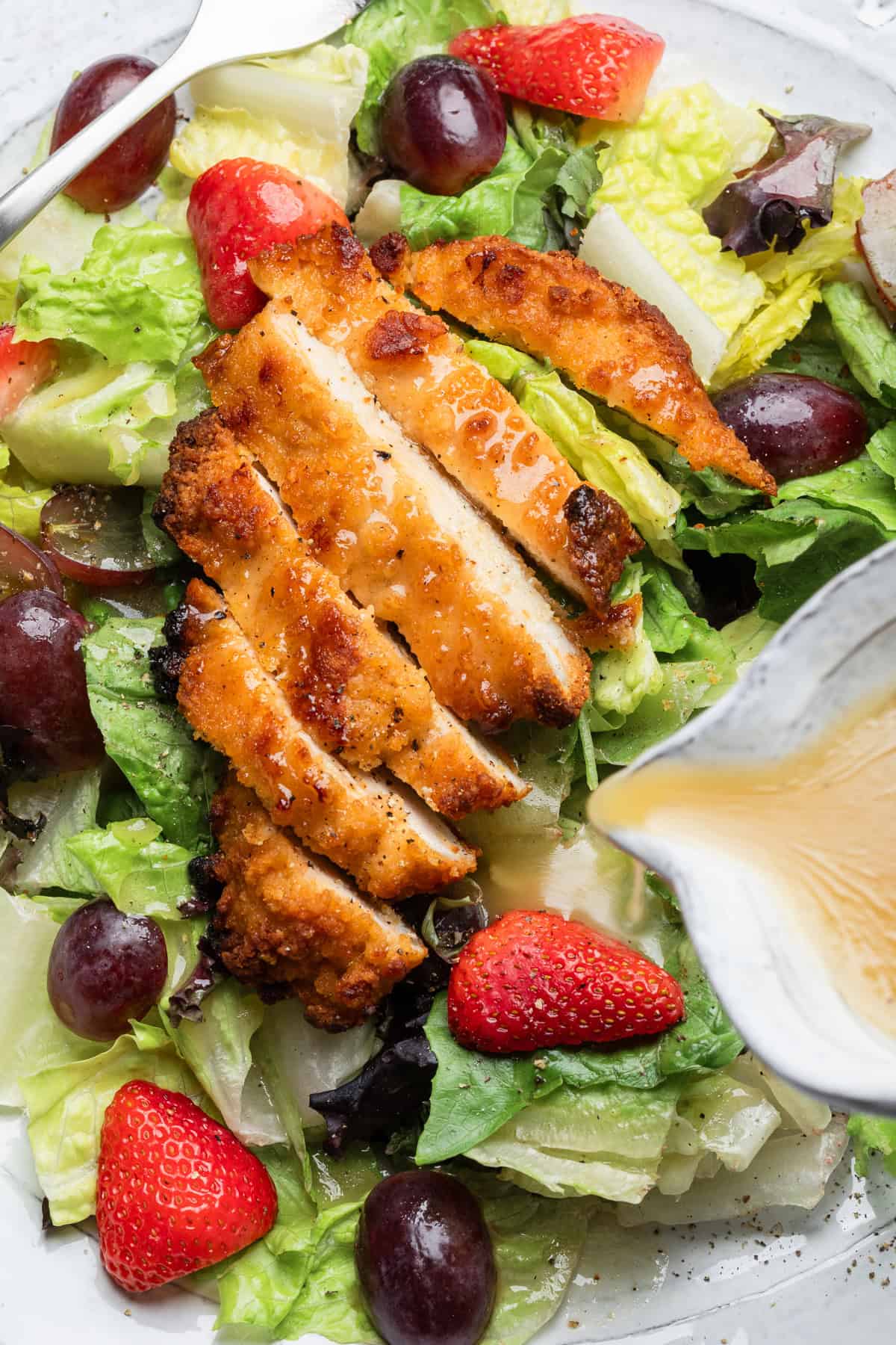 Pouring honey mustard over chicken on a salad.
