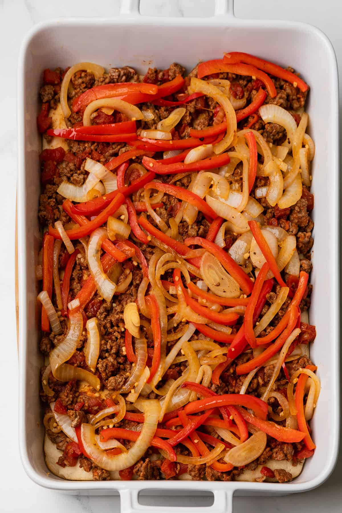 Add cooked onions and red peppers to ground beef layer in baking dish.