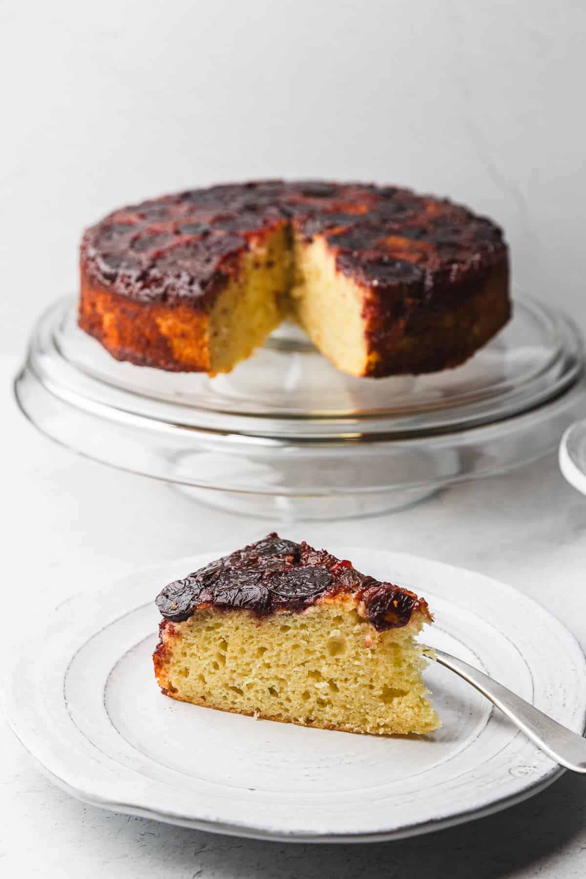 Cherry upside down cake on a stand and a slice on a plate.