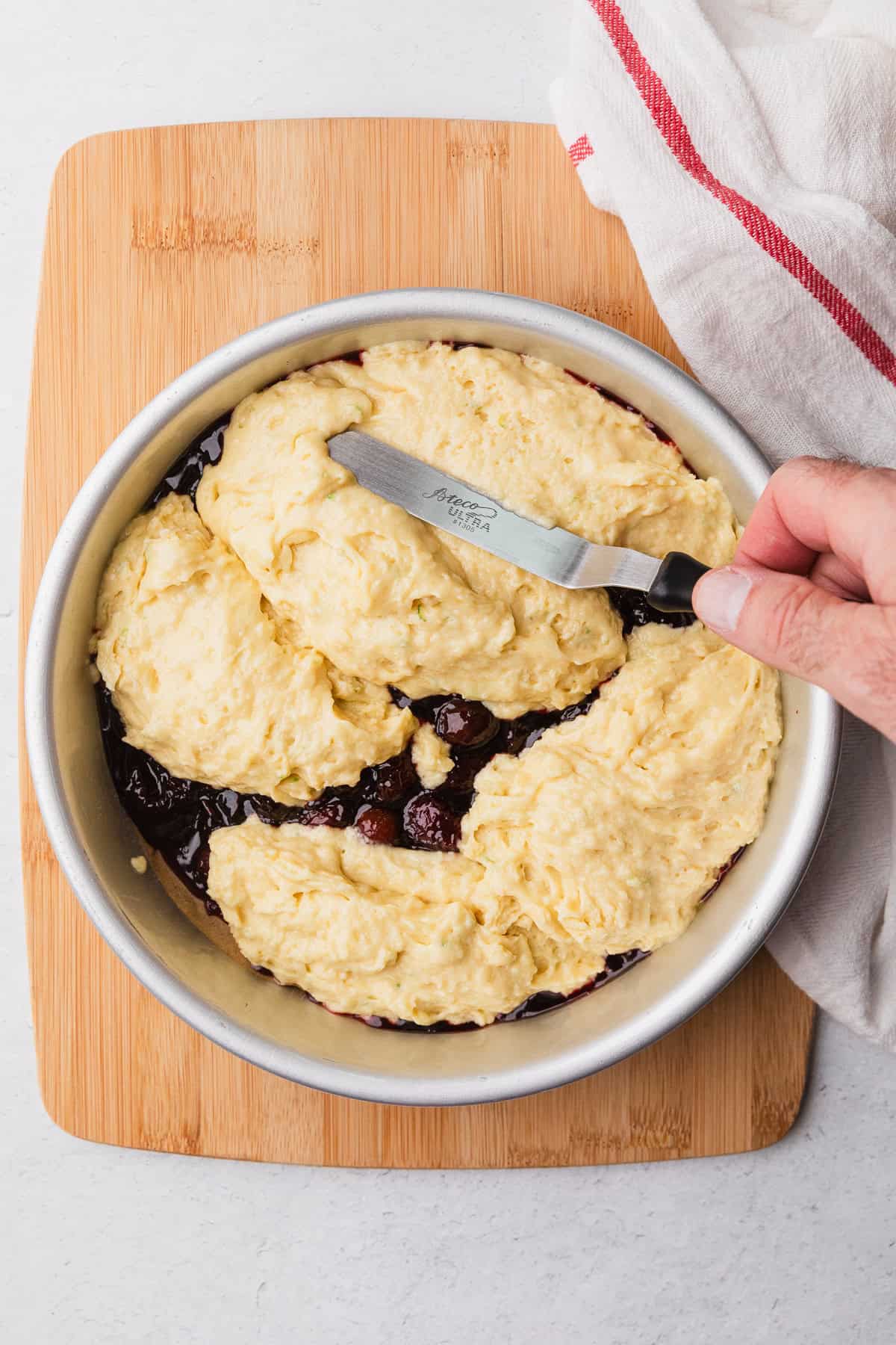Spreading cake batter over cooked cherries.