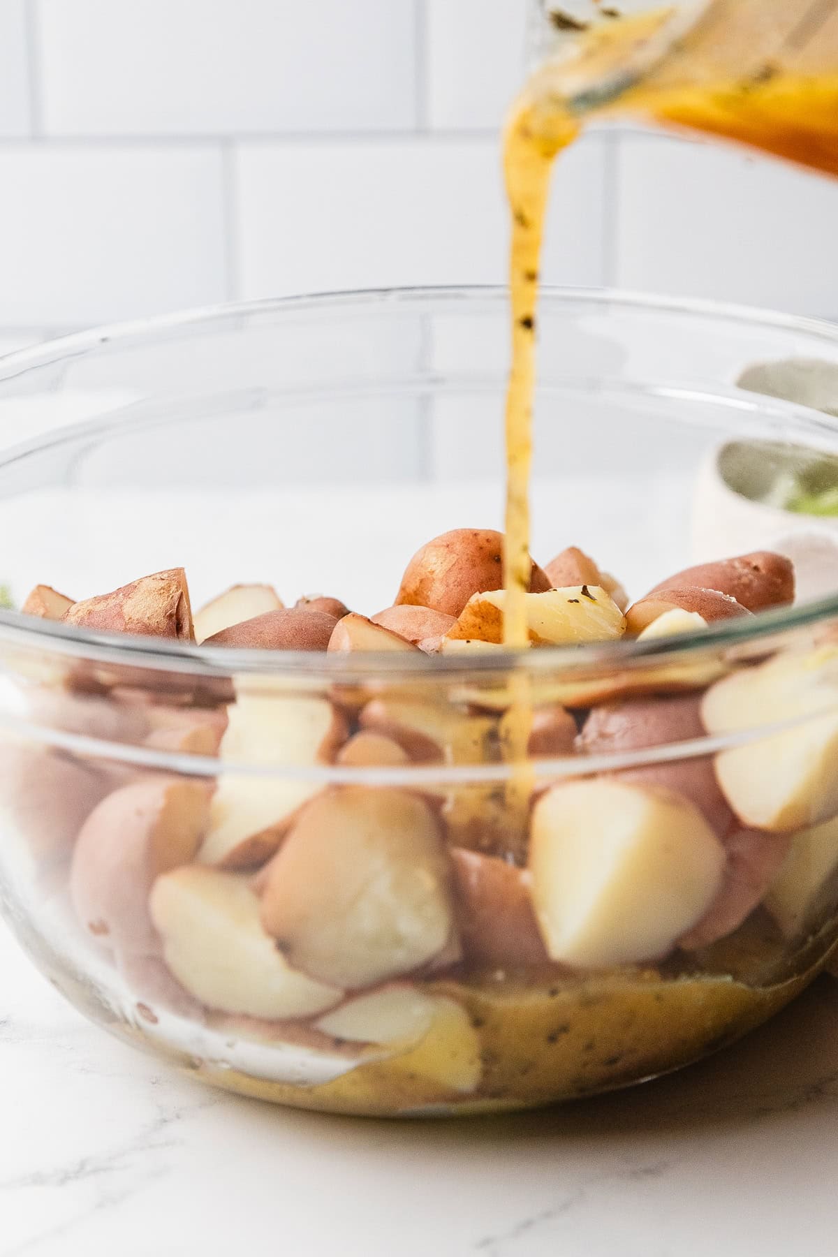 Adding greek vinaigrette to cooked potatoes.