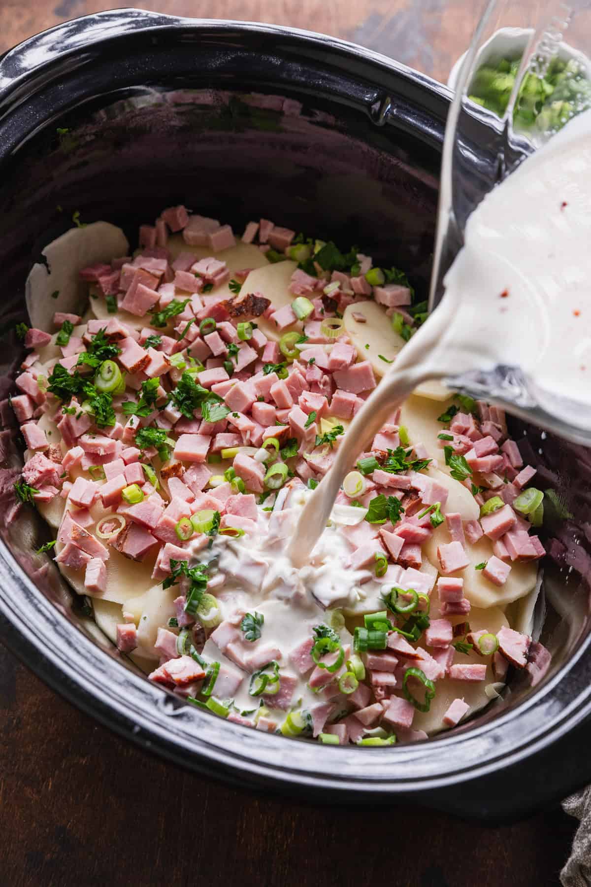 Pouring creamy milk mixture over the layered potatoes and ham mixture.