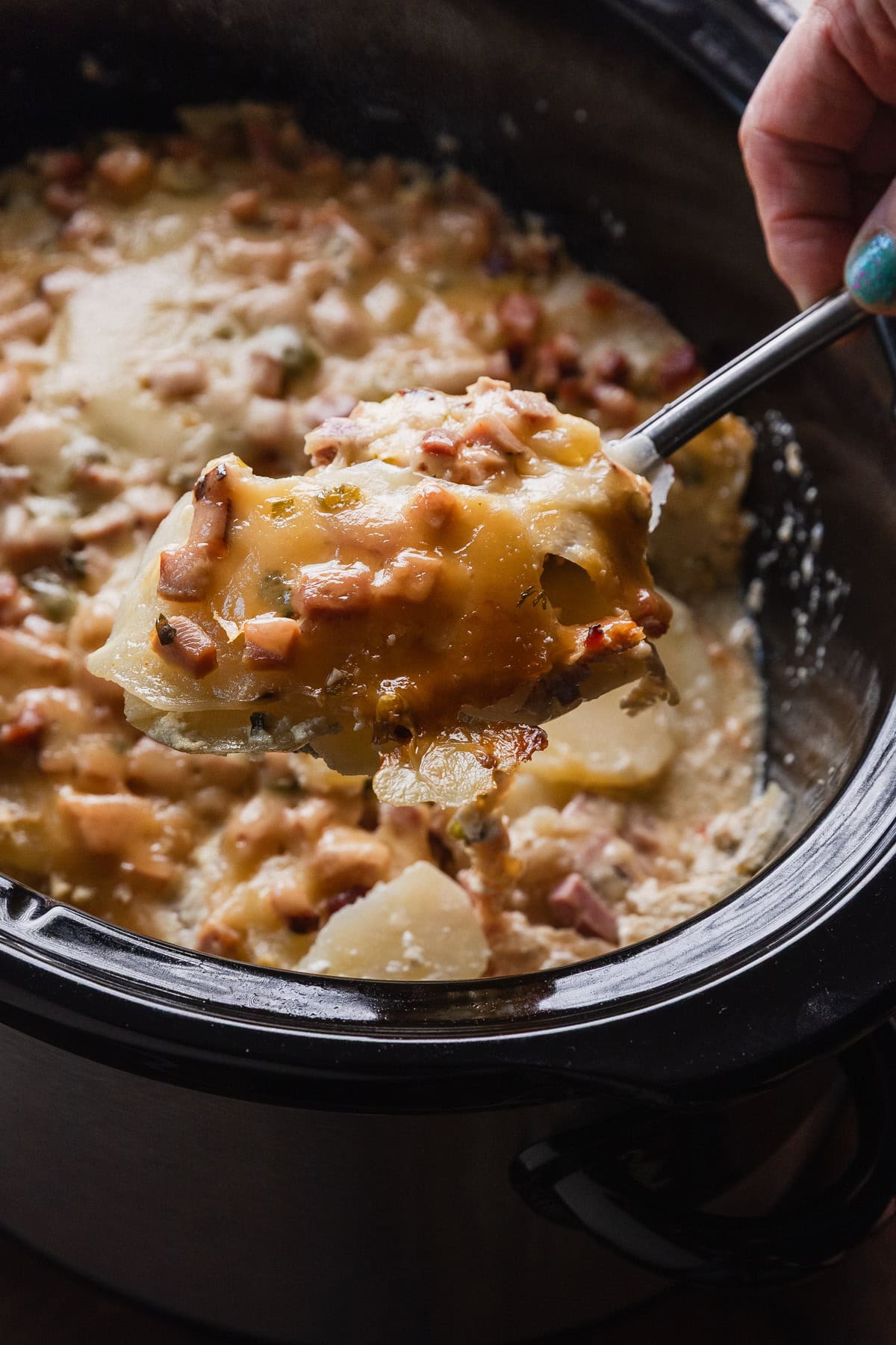 Taking a spoonful of the completed scalloped potatoes and ham from the crockpot.