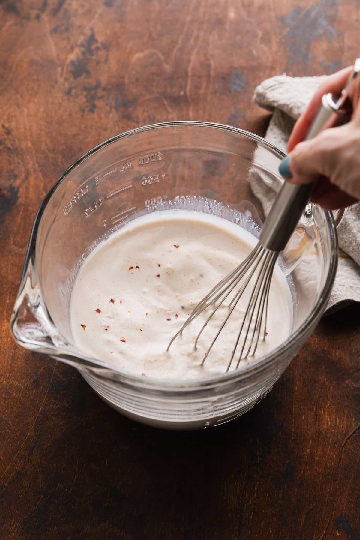 Mixing milk and cream and seasoning to make a creamy sauce.
