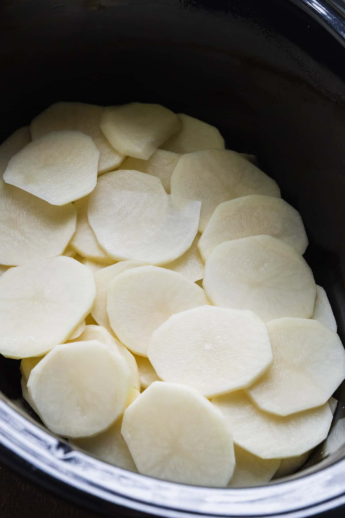 Thinly sliced potatoes layered in a crockpot.