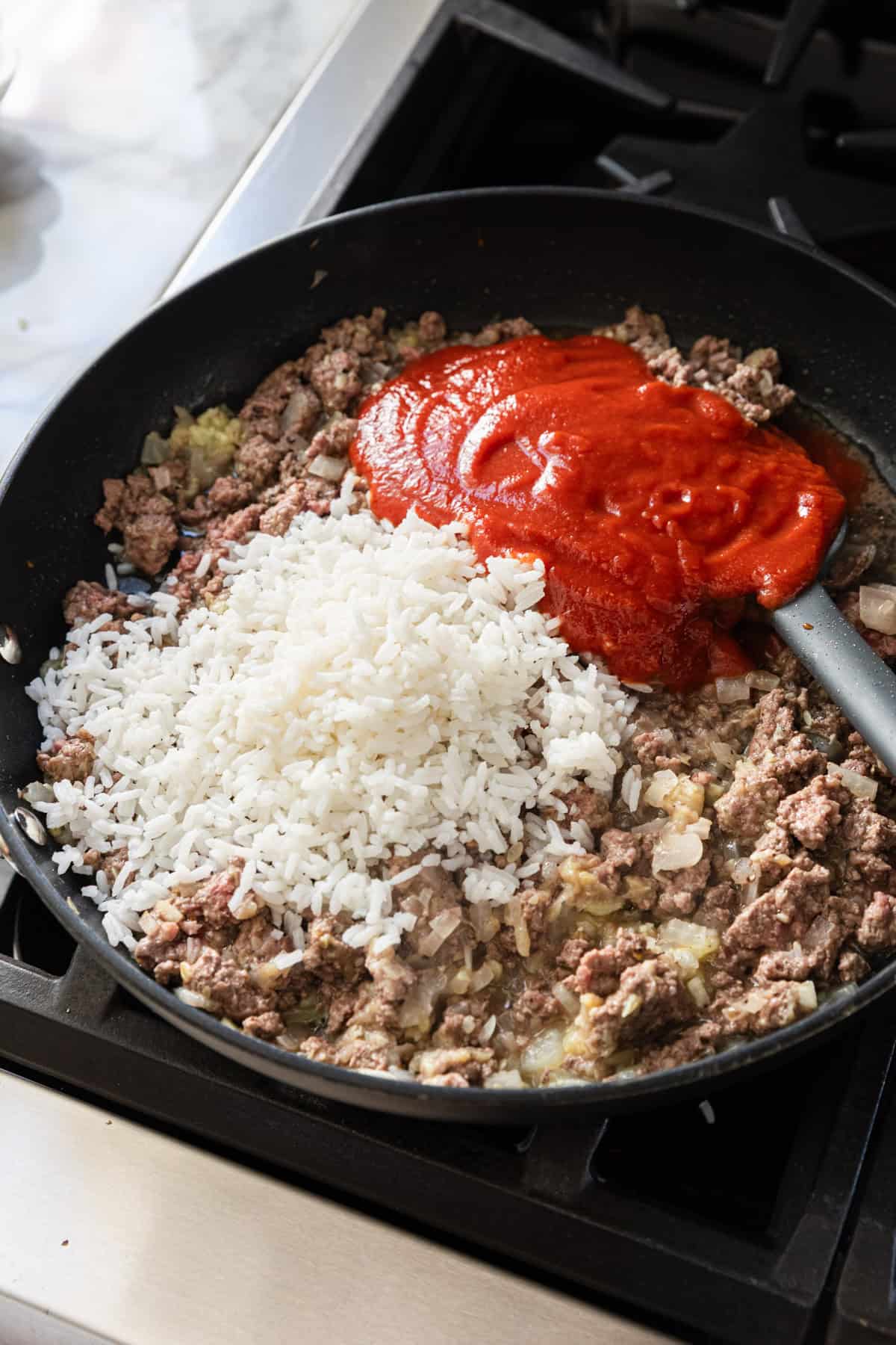 Adding rice and tomato sauce to the skillet.