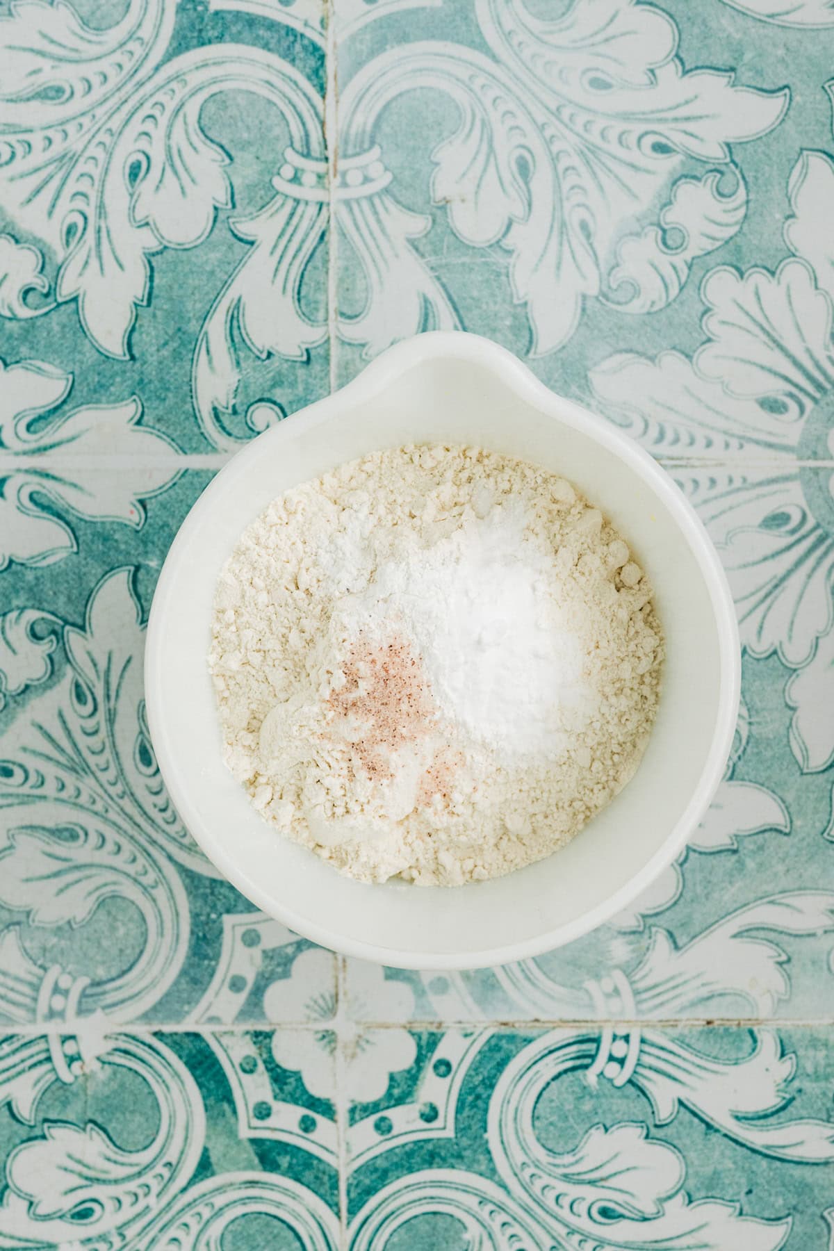 A bowl of flour and sugar on a blue and white tile.