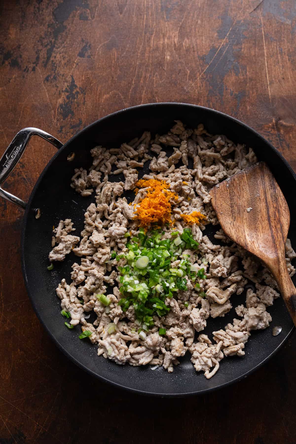 Adding orange rind and green onions to cooked ground chicken.