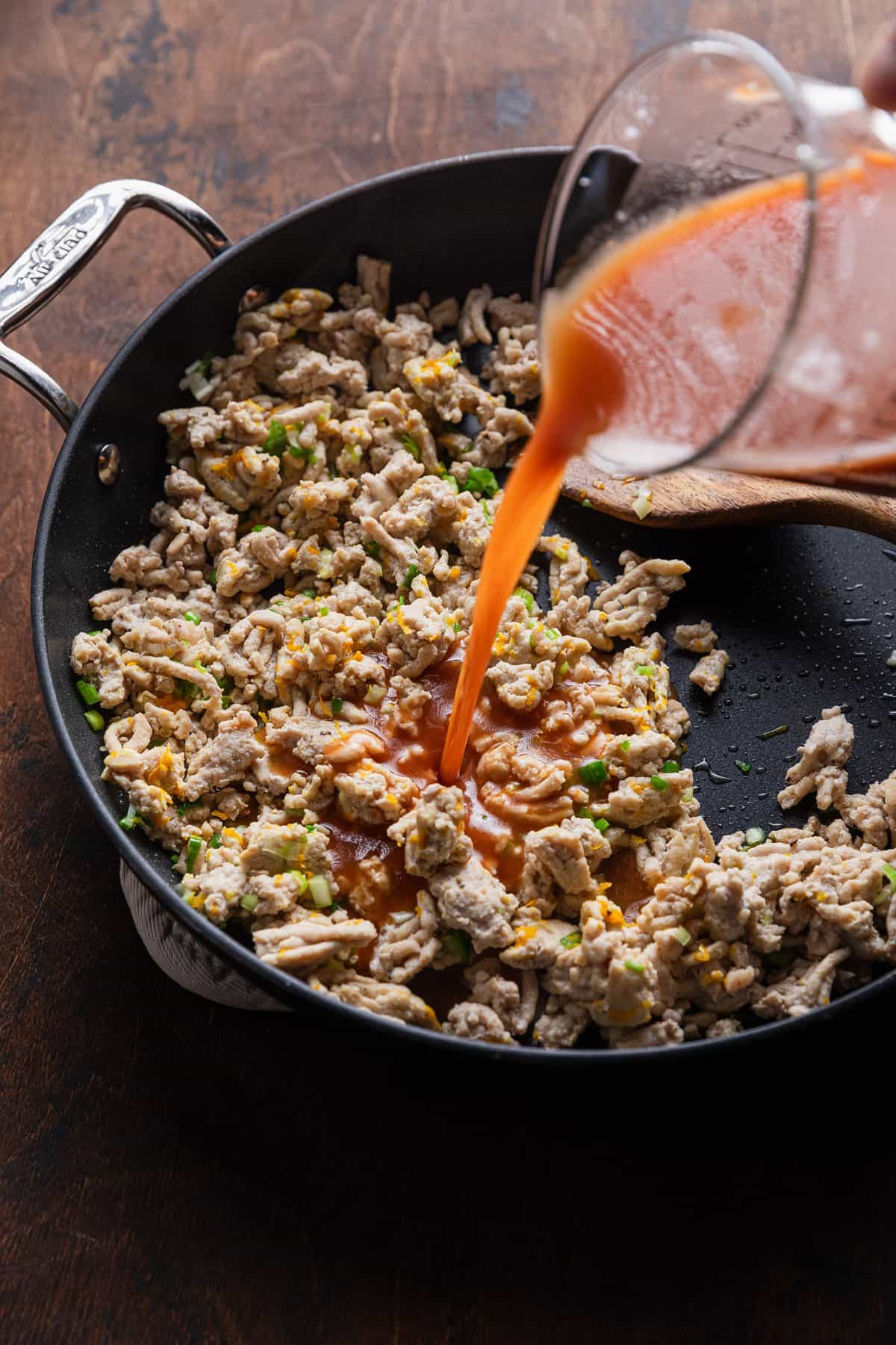 Adding orange sauce to cooked meat.