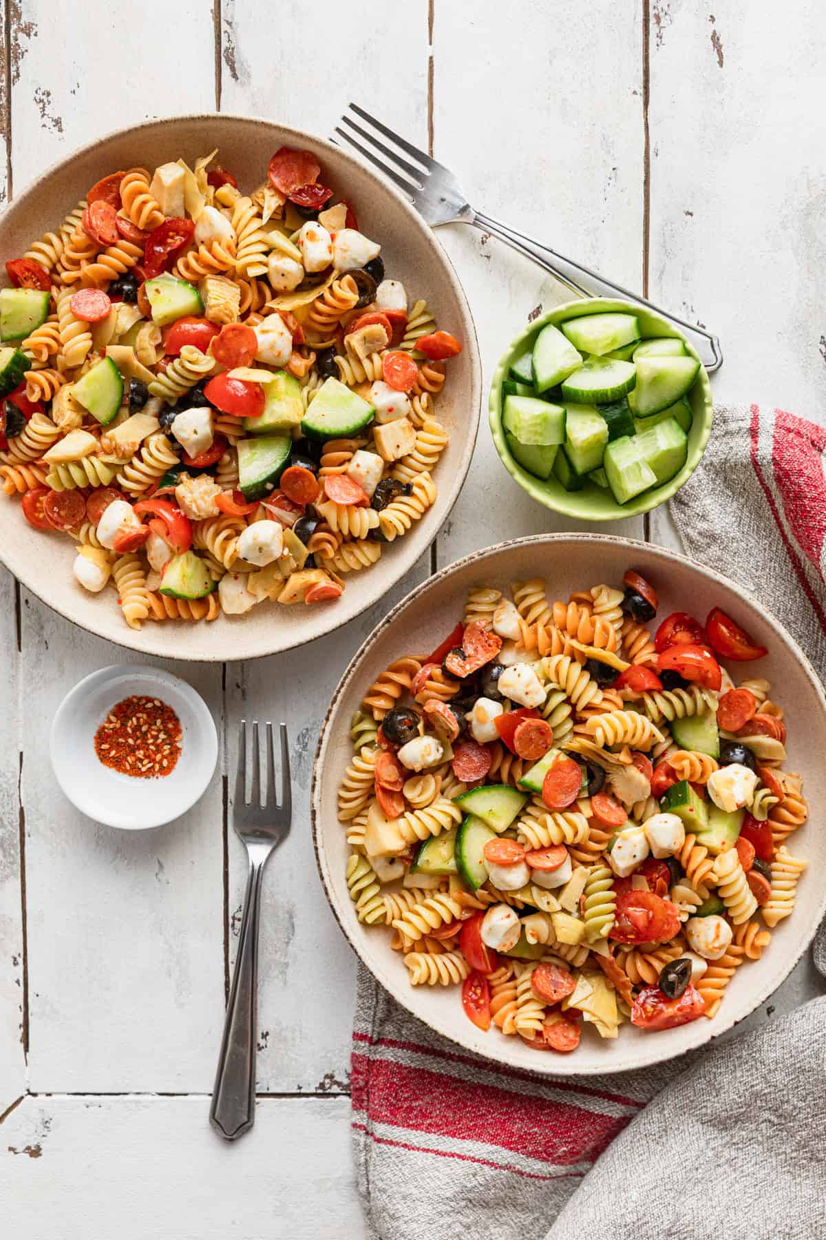 a bowl and plate filled with Italian dressing pasta salad with pine nuts in a small bowl Two bowls of zesty Italian dressing pasta salad.