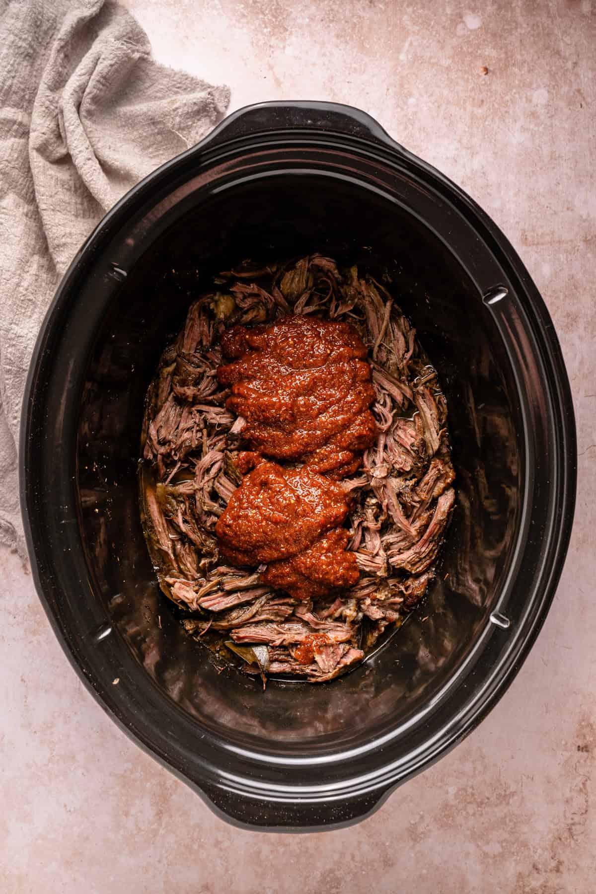 Adding ranchero sauce to the shredded barbacoa.