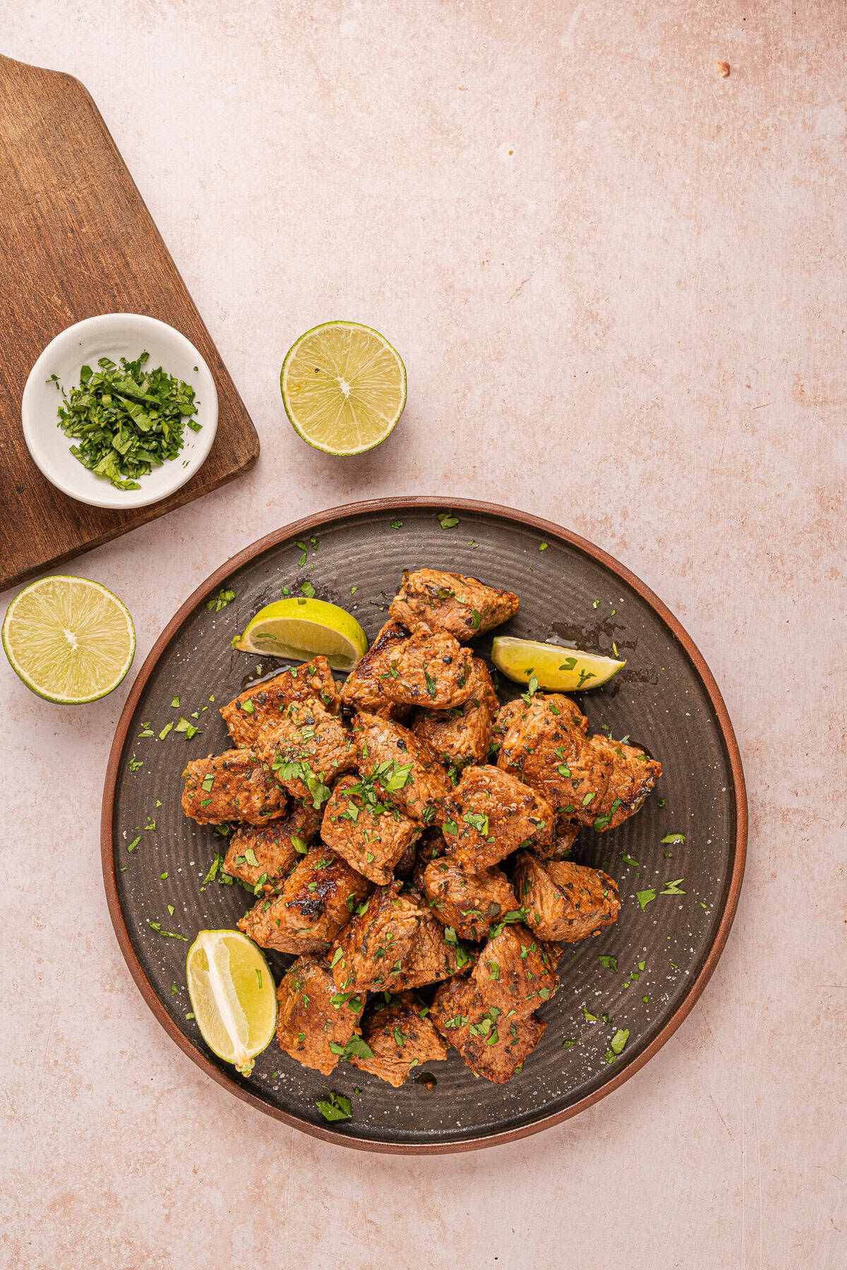 A plate of steak bites with lime wedges.
