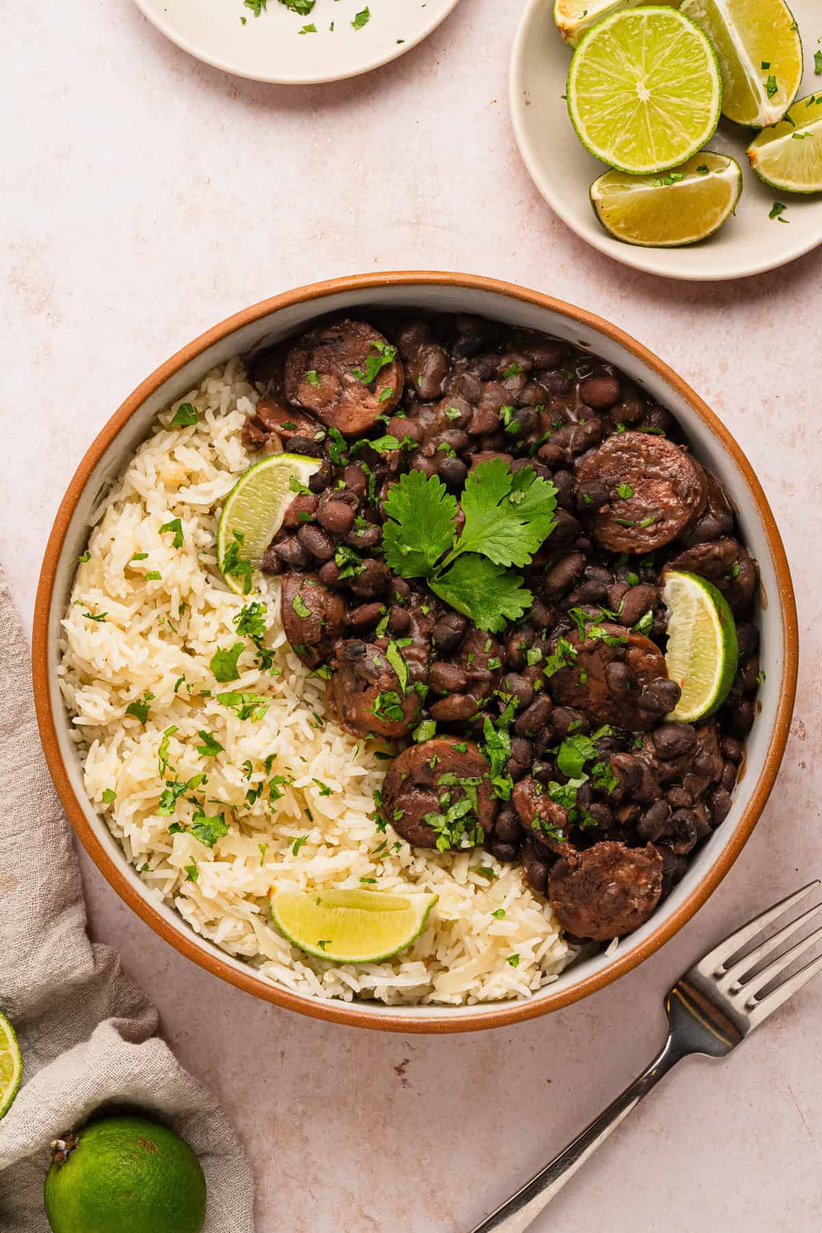 Bowl of black beans, sausage, and rice with limes as garnish.