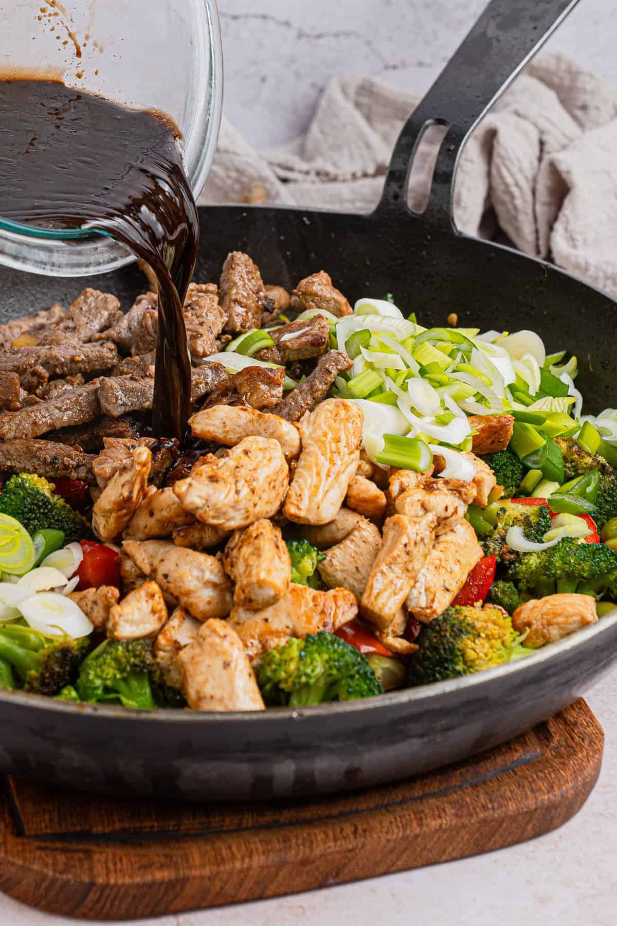 Adding stir fry sauce to the skillet with ingredients.