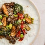 Chicken and steak stir fry over white rice with sesame seeds garnish.