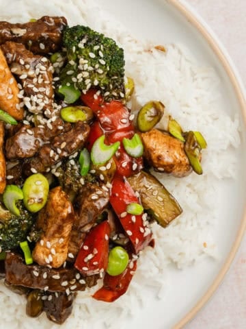 Chicken and steak stir fry over white rice with sesame seeds garnish.