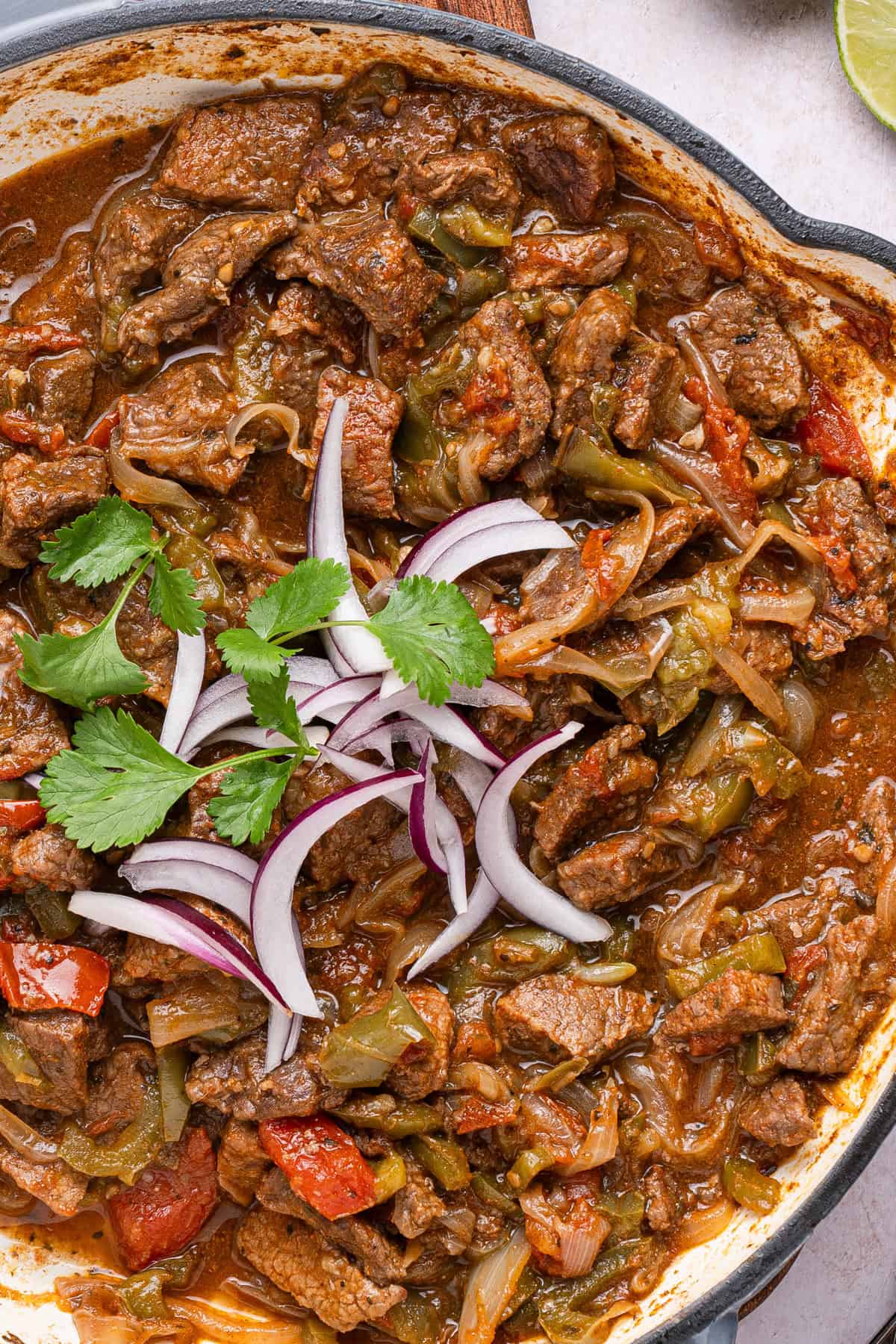 The completed steak picado cooked in a skillet with some sliced red onion and cilantro.