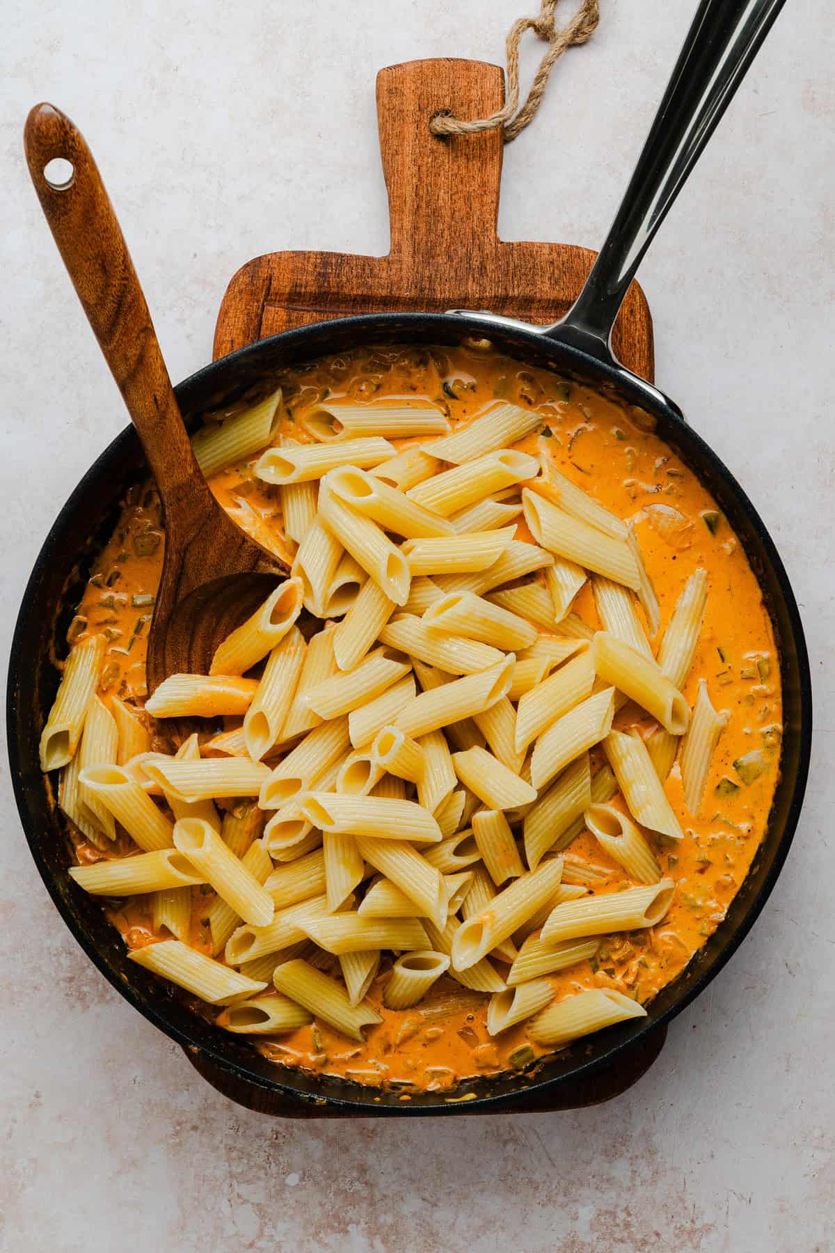 Adding pasta to the sauce.