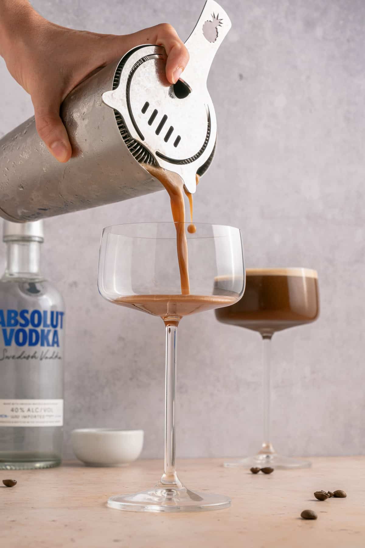 Pouring shaken martini into coupe glasses.