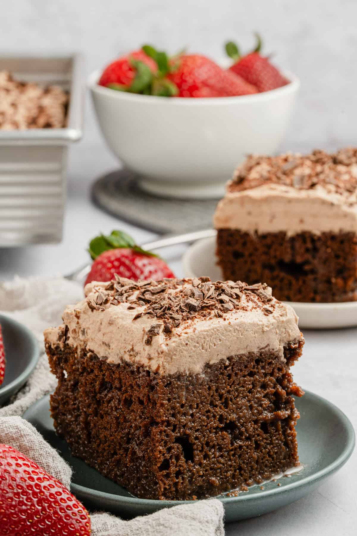 Chocolate tres leches cake on a plate with a strawberry on top.