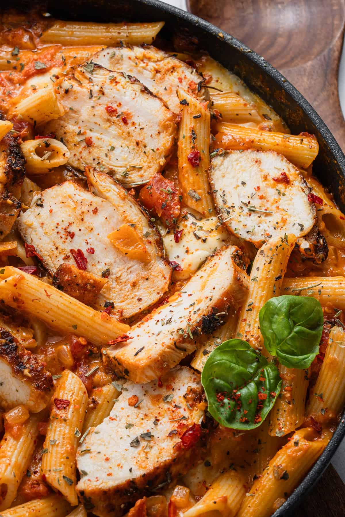 The completed recipe of cooked chicken breast over penne pasta with vodka sauce.