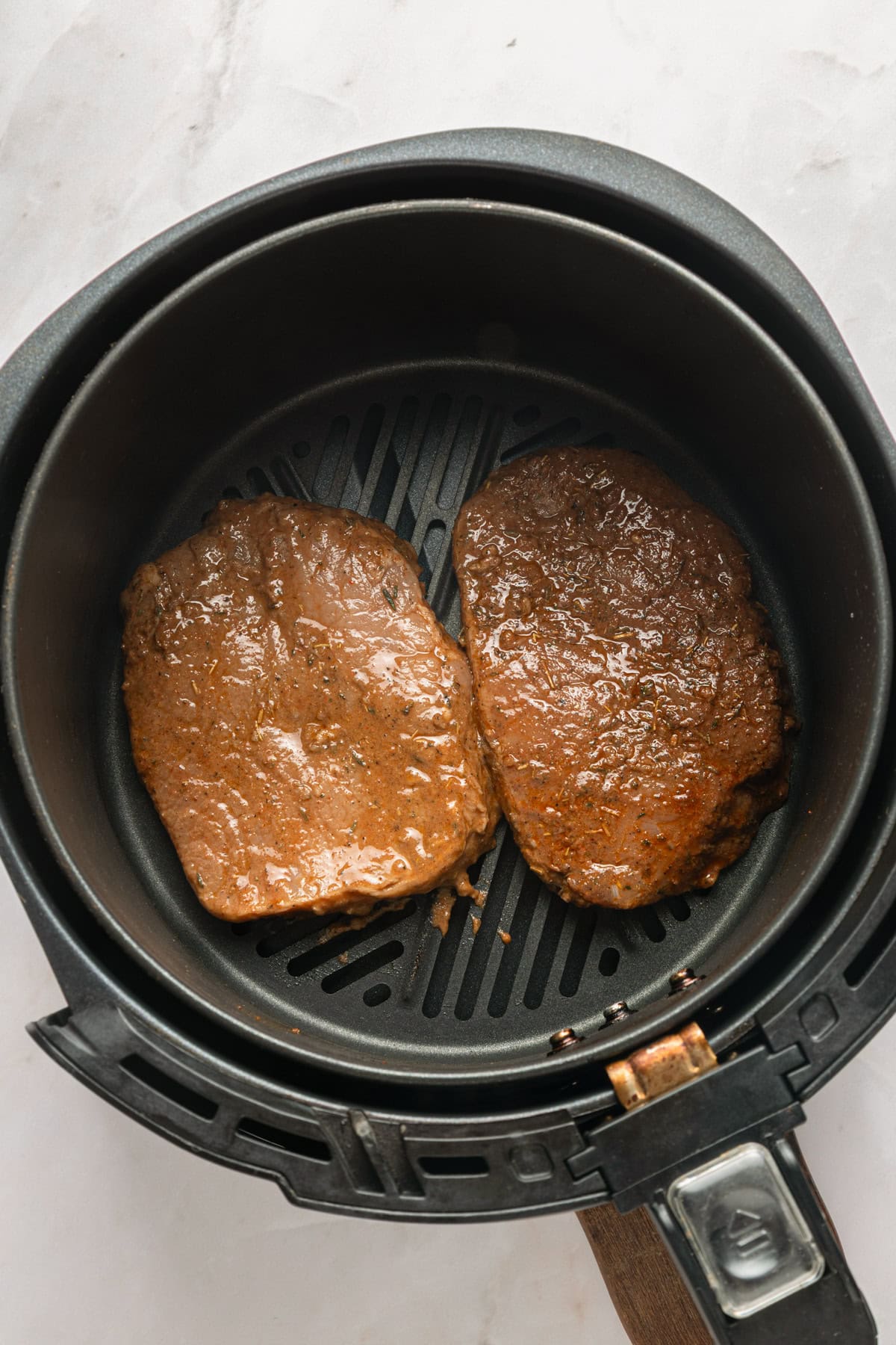 Boneless pork chops after marinating and in the air fryer basket.