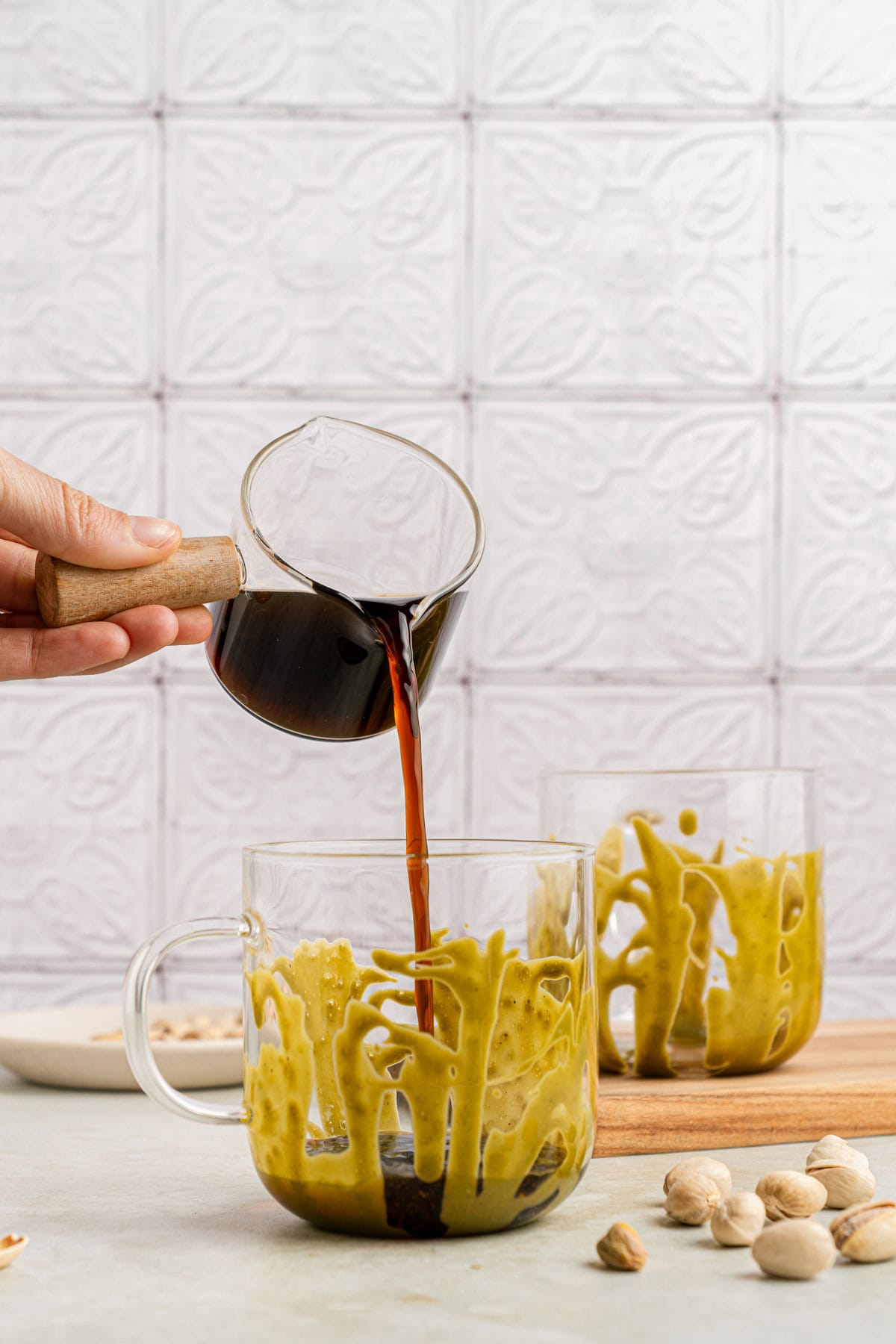 Pouring espresso into clear mugs that have been drizzled with pistachio cream.