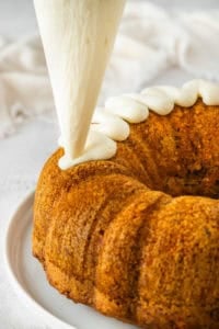 Piping cream cheese frosting on cake.