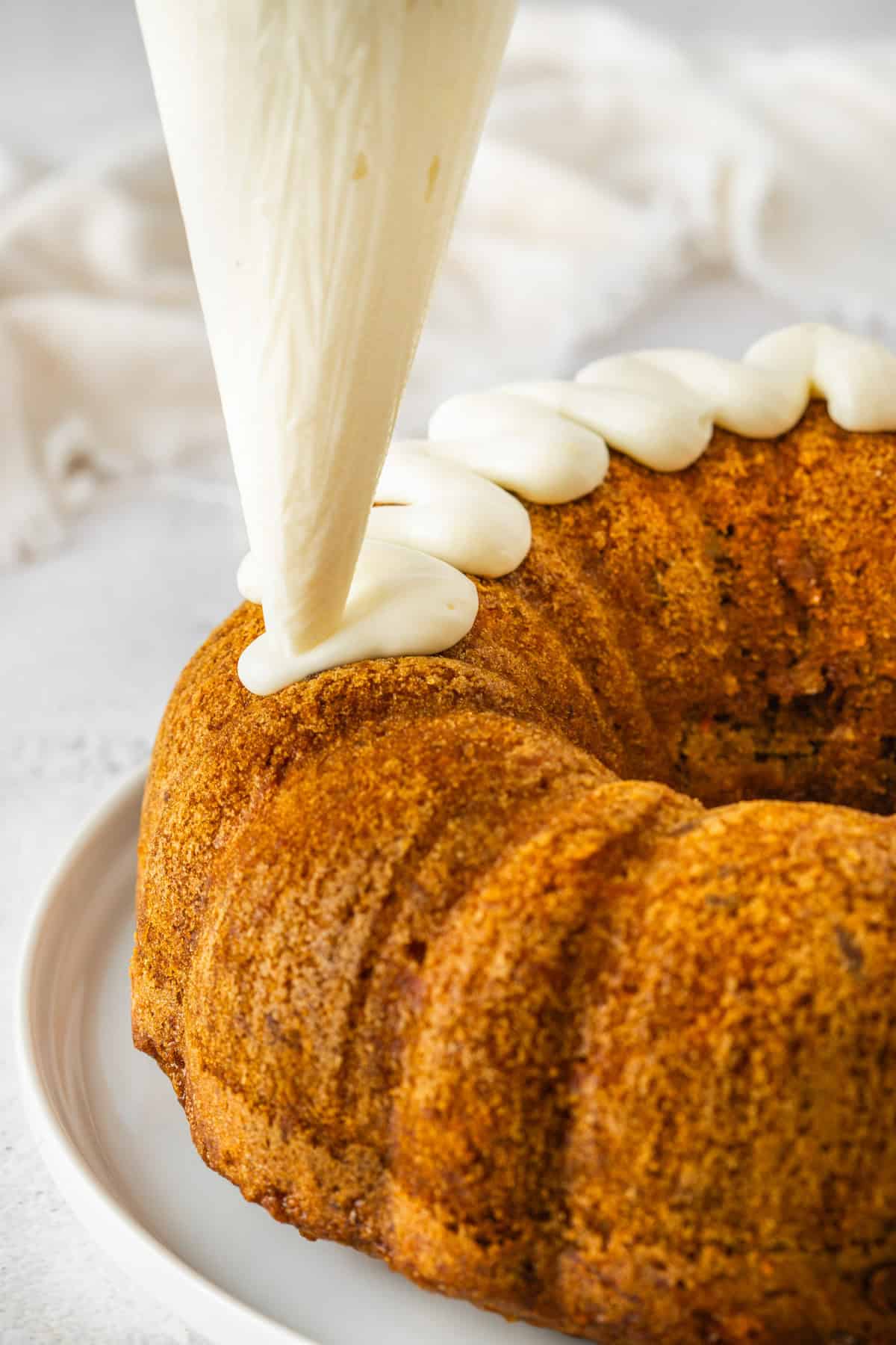 Piping cream cheese frosting on cake.