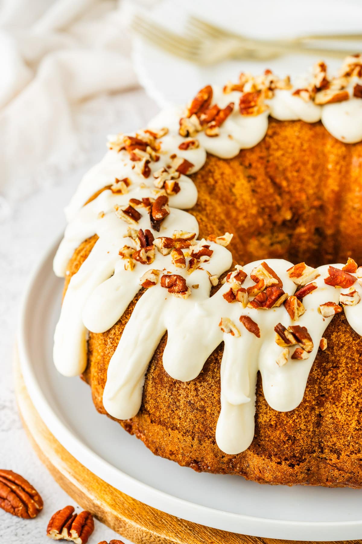 Carrot bundt cake with cream cheese frosting and chopped pecan topping.