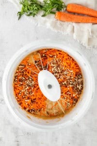 Adding chopped pecans a grated carrot to bowl.