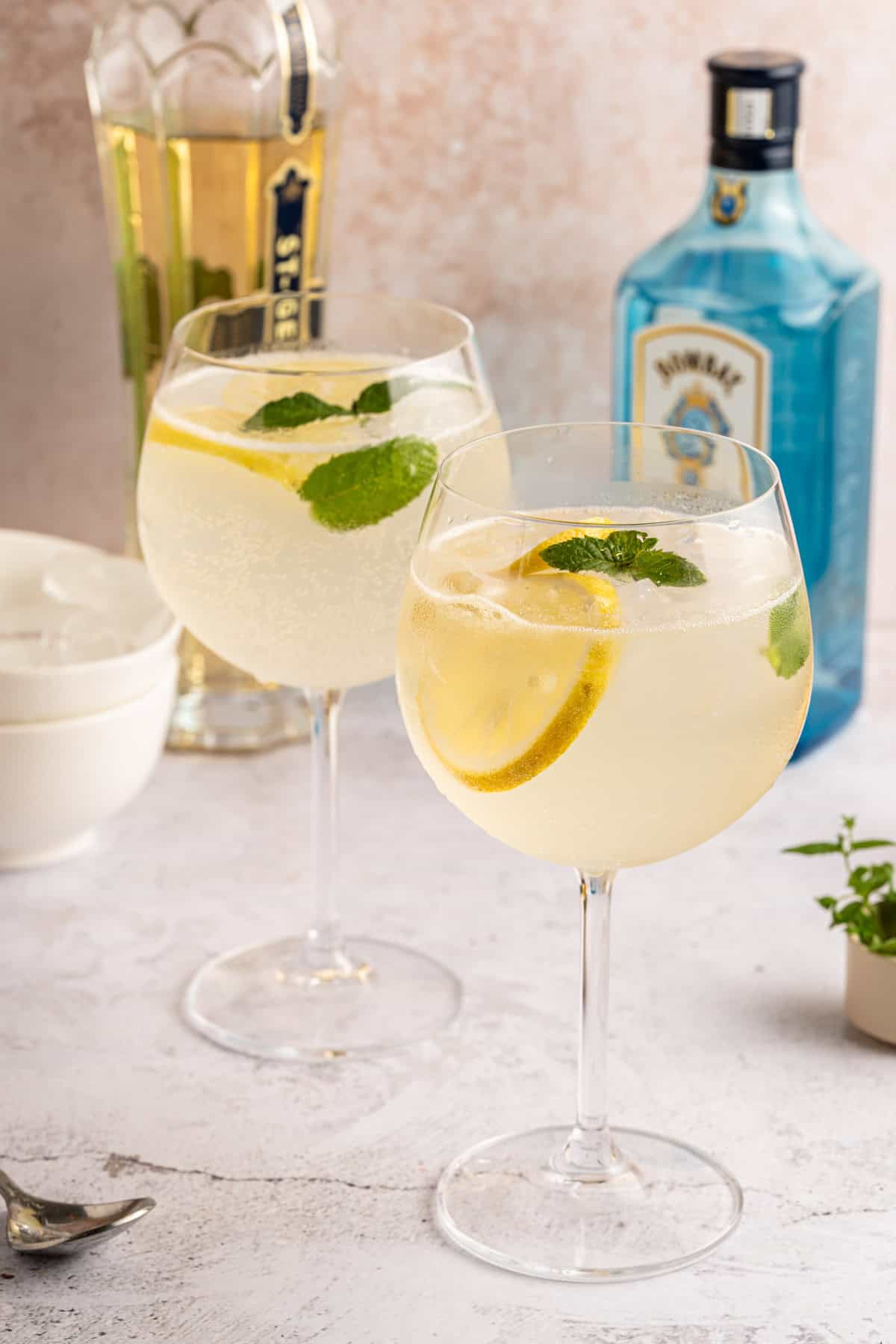 A gin and edlerflower liquor cocktail in a wine glass with a lemon and mint garnish.